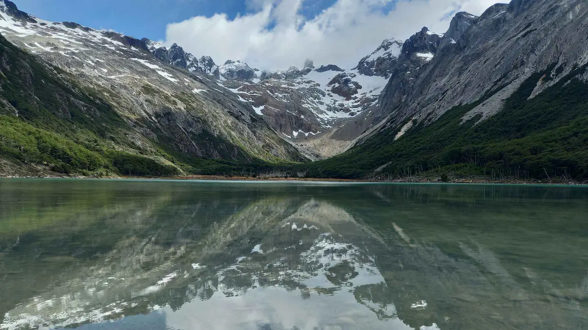 Trekking group walking through peat bogs toward the green water of Laguna Esmeralda above the Valle de Tierra Mayor near Ushuaia, Argentina